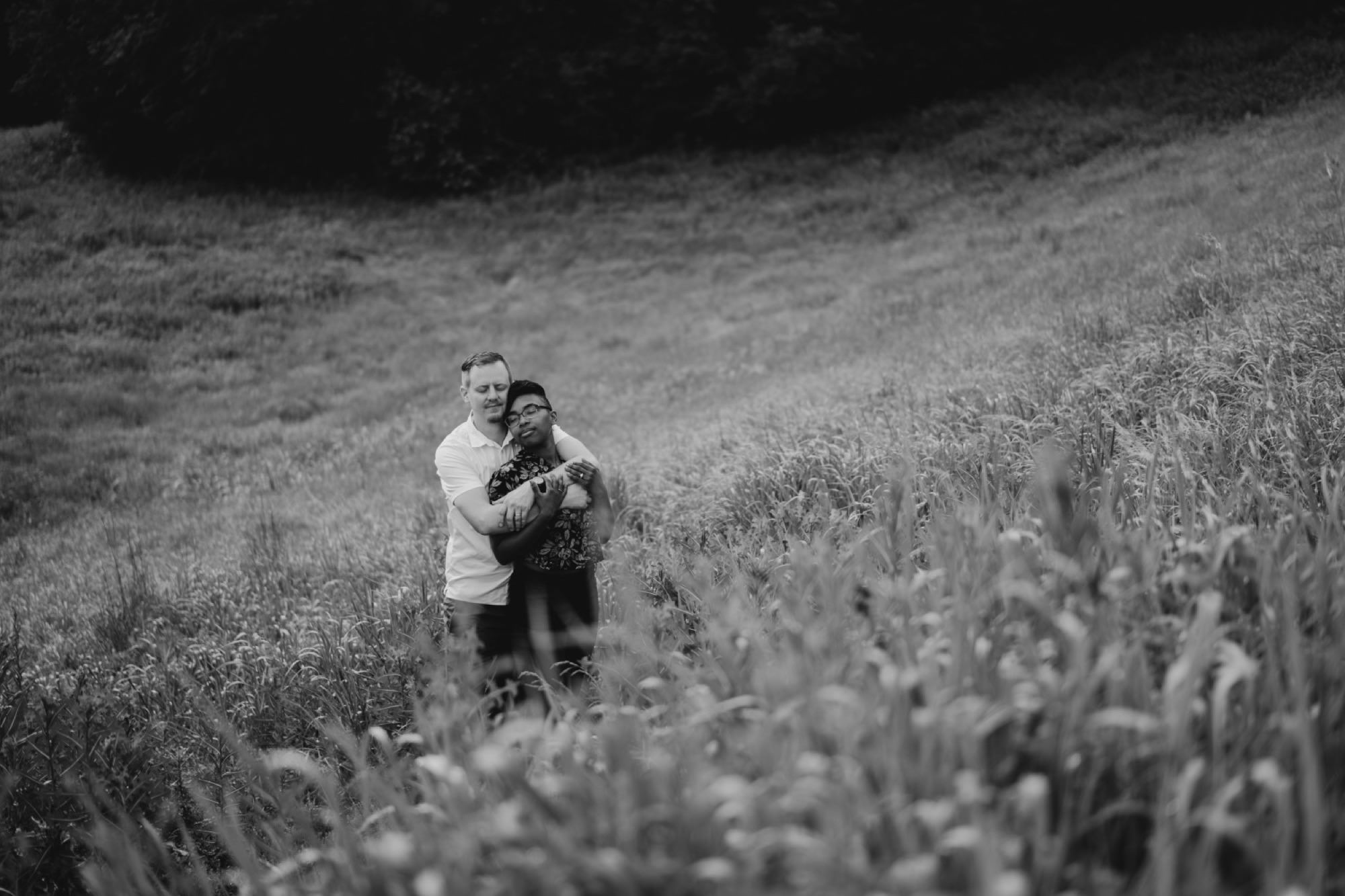 couple cuddling in field with eyes closed in black hoof park