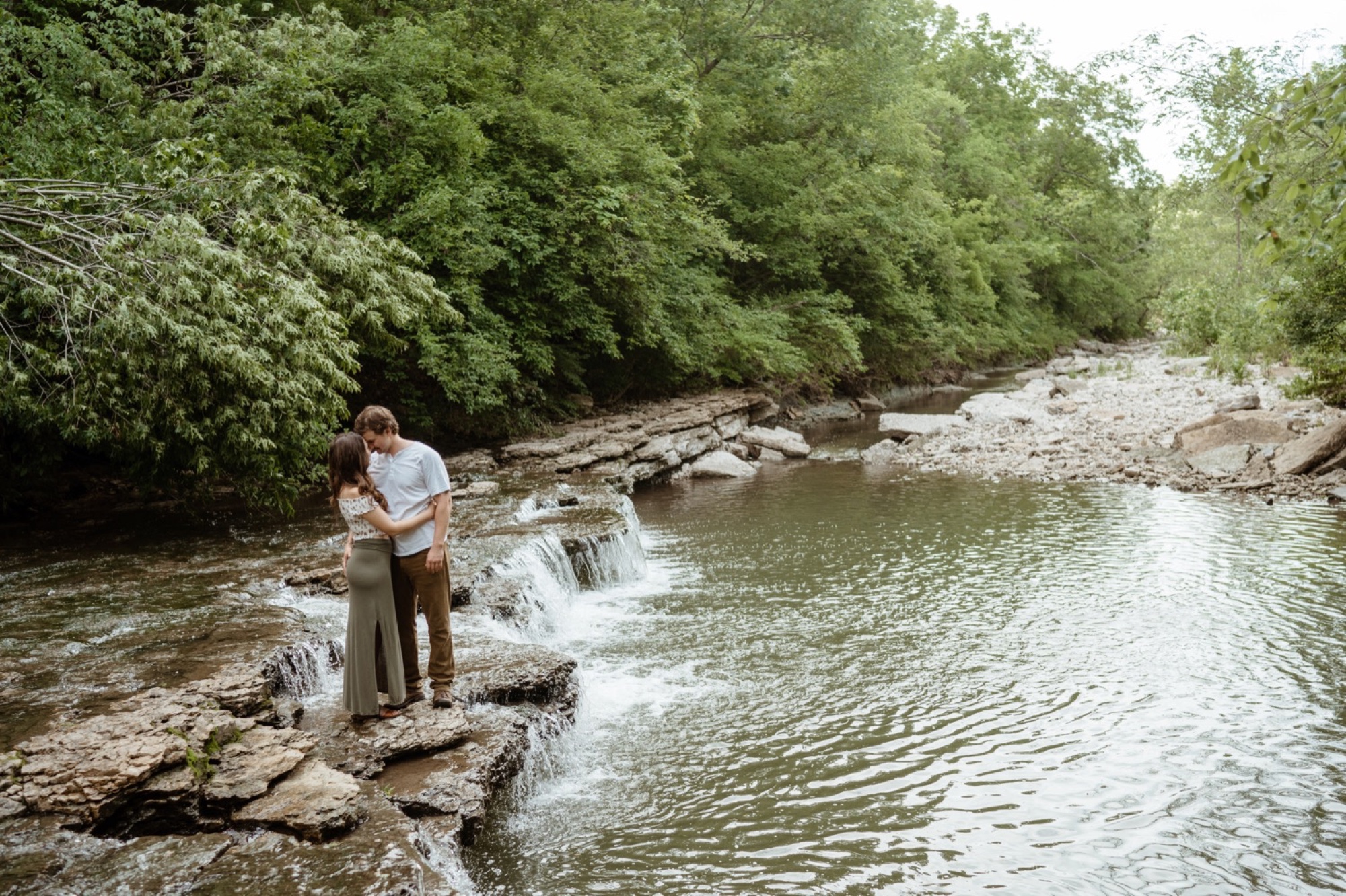 couple stands at edge of creek for their winterset engagement session