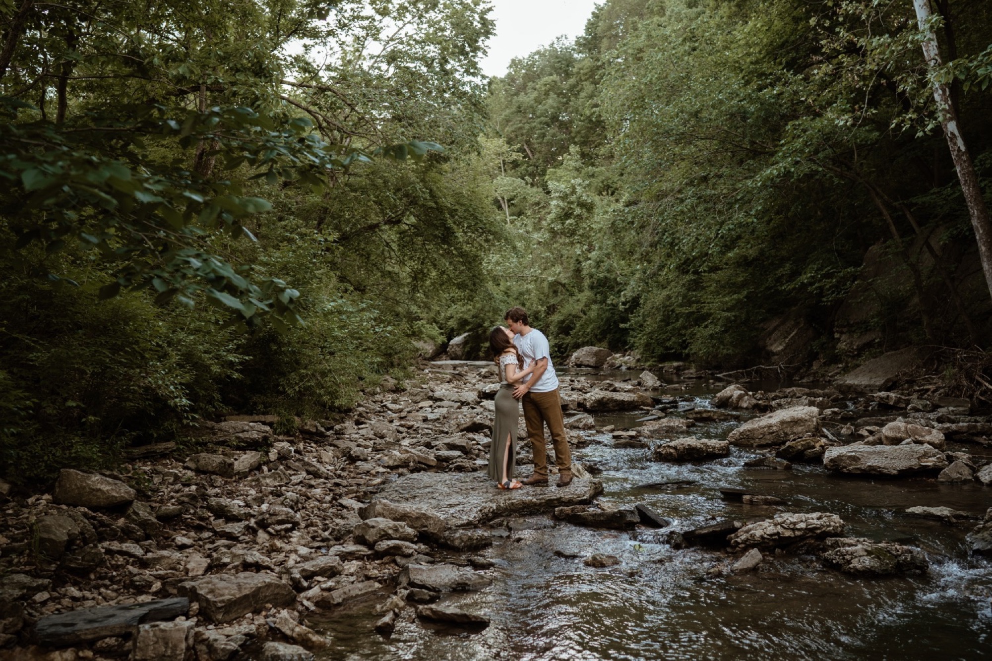 couple standing in middle of creek kissing during winterset engagement session