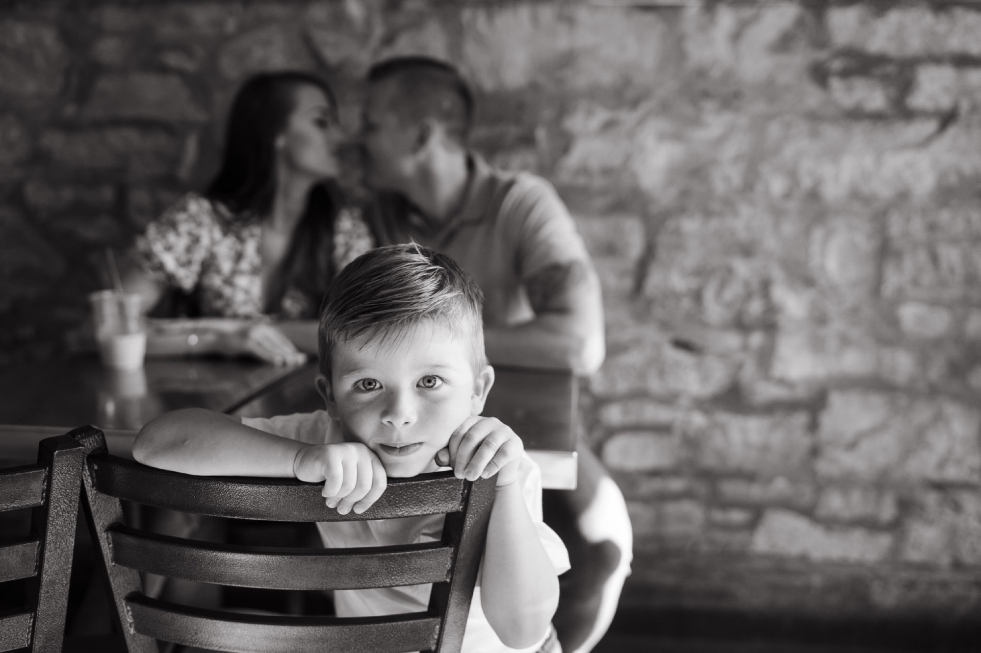 parents cuddled up in back of photo while child looks at camera during parkville coffee engagement session