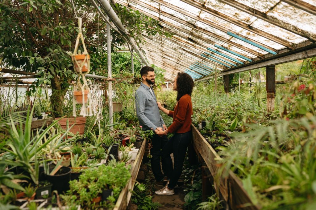 couple holds hands and smiles in greenhouse