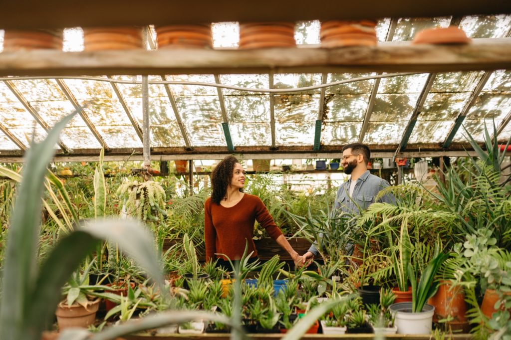 Clients hold hands and walk through John's Greenhouse Engagement Session
