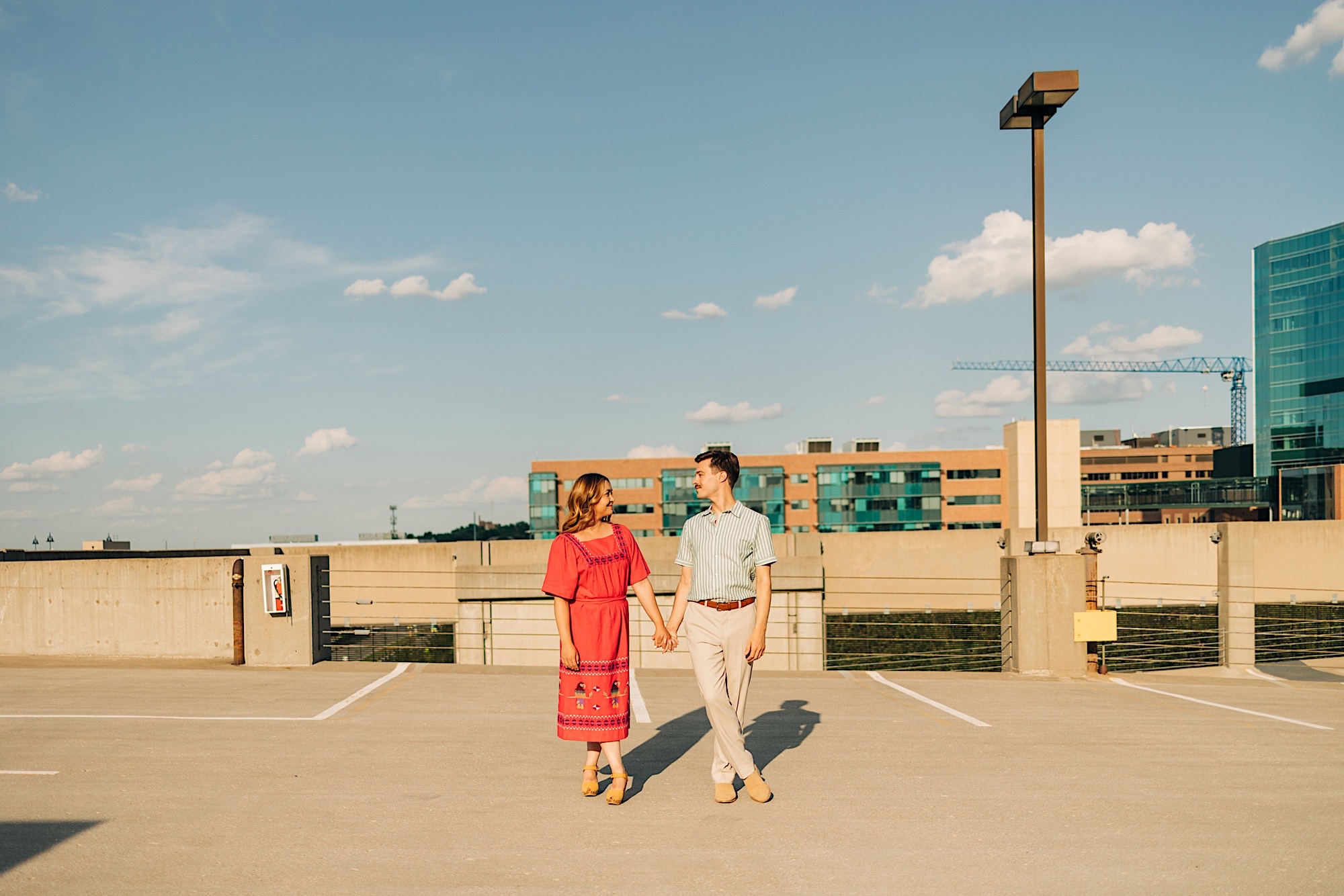Couple stands in afternoon harsh sun holding hands at Sheraton Parking Engagement Session