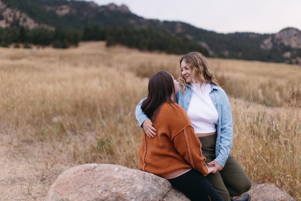Two women snuggle on a rock and look into each other's eyes at Chautauqua Park Engagement Session